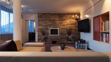 A modern living room with a sofa, a coffee table, a flat-screen TV, a bookshelf, and a fireplace.