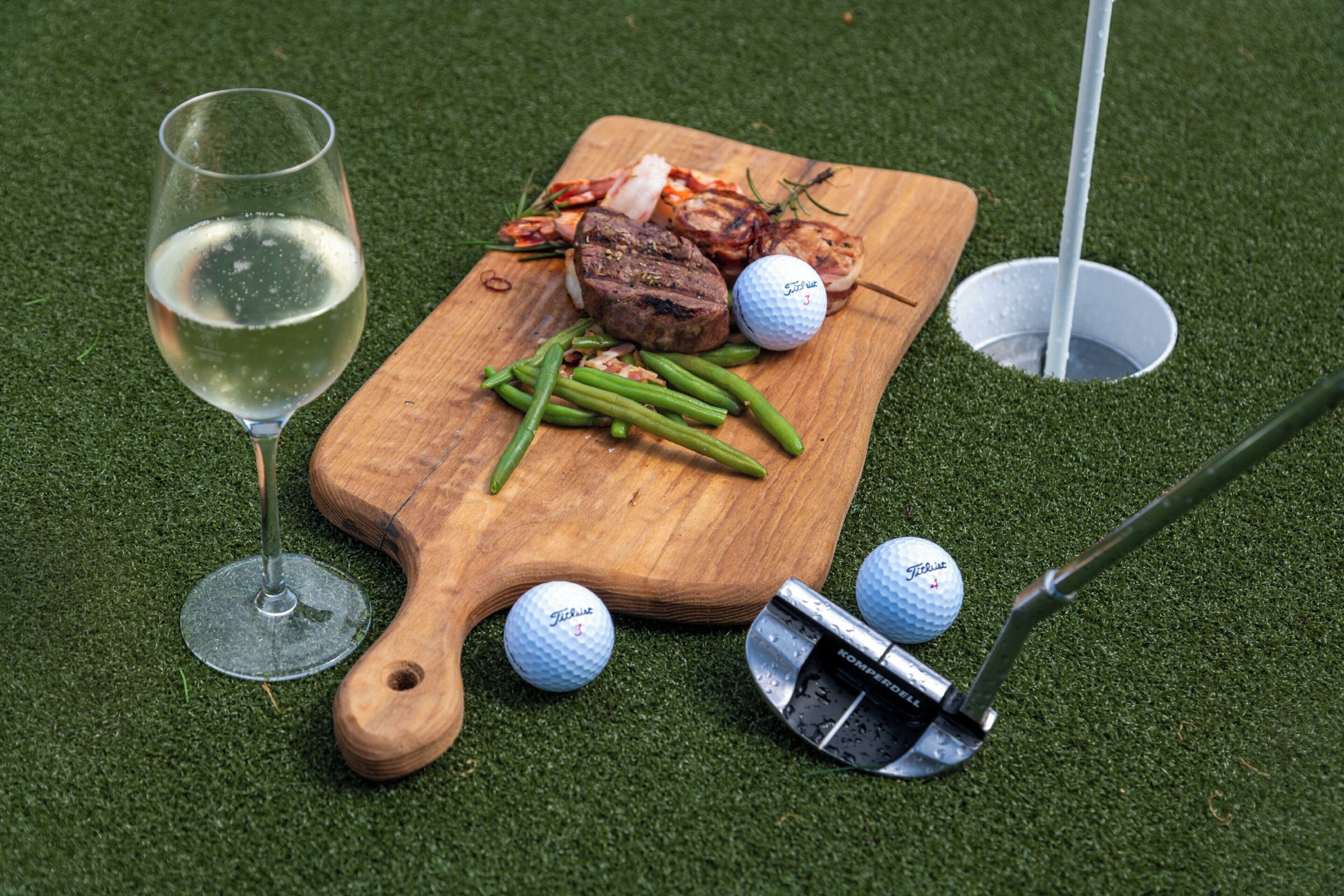 Una tabla de madera con comida y pelotas de golf sobre una superficie verde.