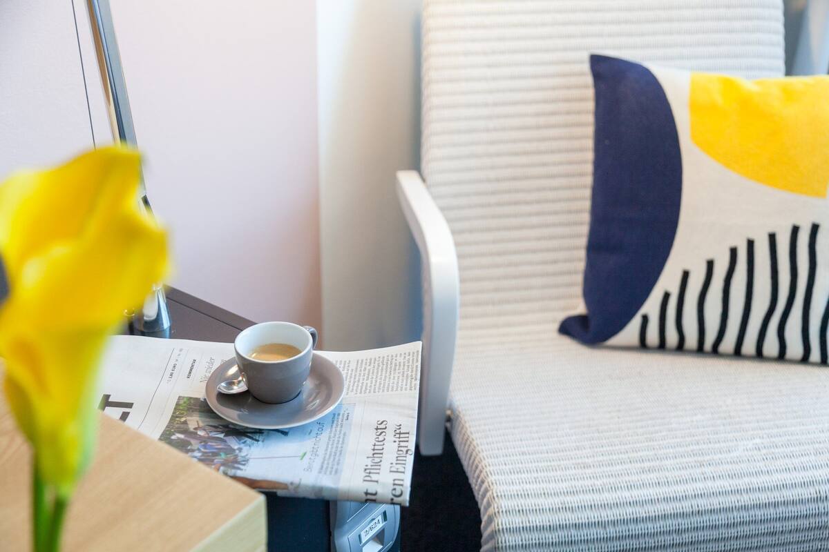 Ein aufgeräumter Leseplatz mit Sessel, Kaffeetasse, Zeitung und Buch.
