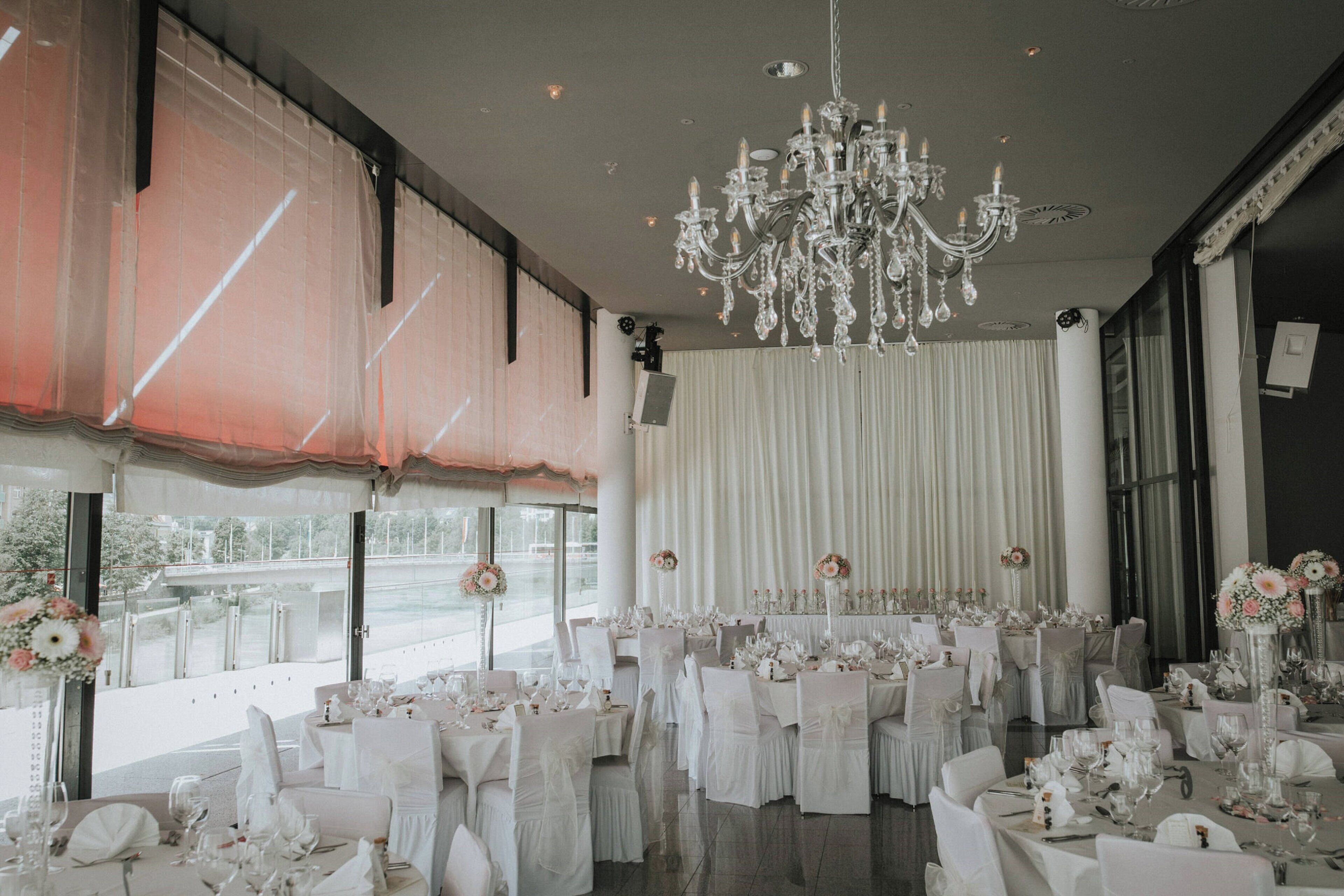 A banquet hall with round tables, white tablecloths, and floral centerpieces.