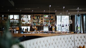 Un bar con una barra alta, varias lámparas colgantes y una variedad de botellas y vasos en estanterías.