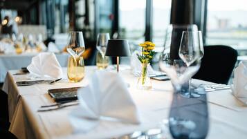 A dining table set with white tablecloth, wine glasses, a vase with yellow flowers, and a black lamp.