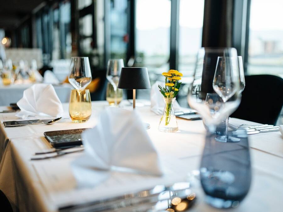 A dining table set with white tablecloth, wine glasses, a vase with yellow flowers, and a black lamp.