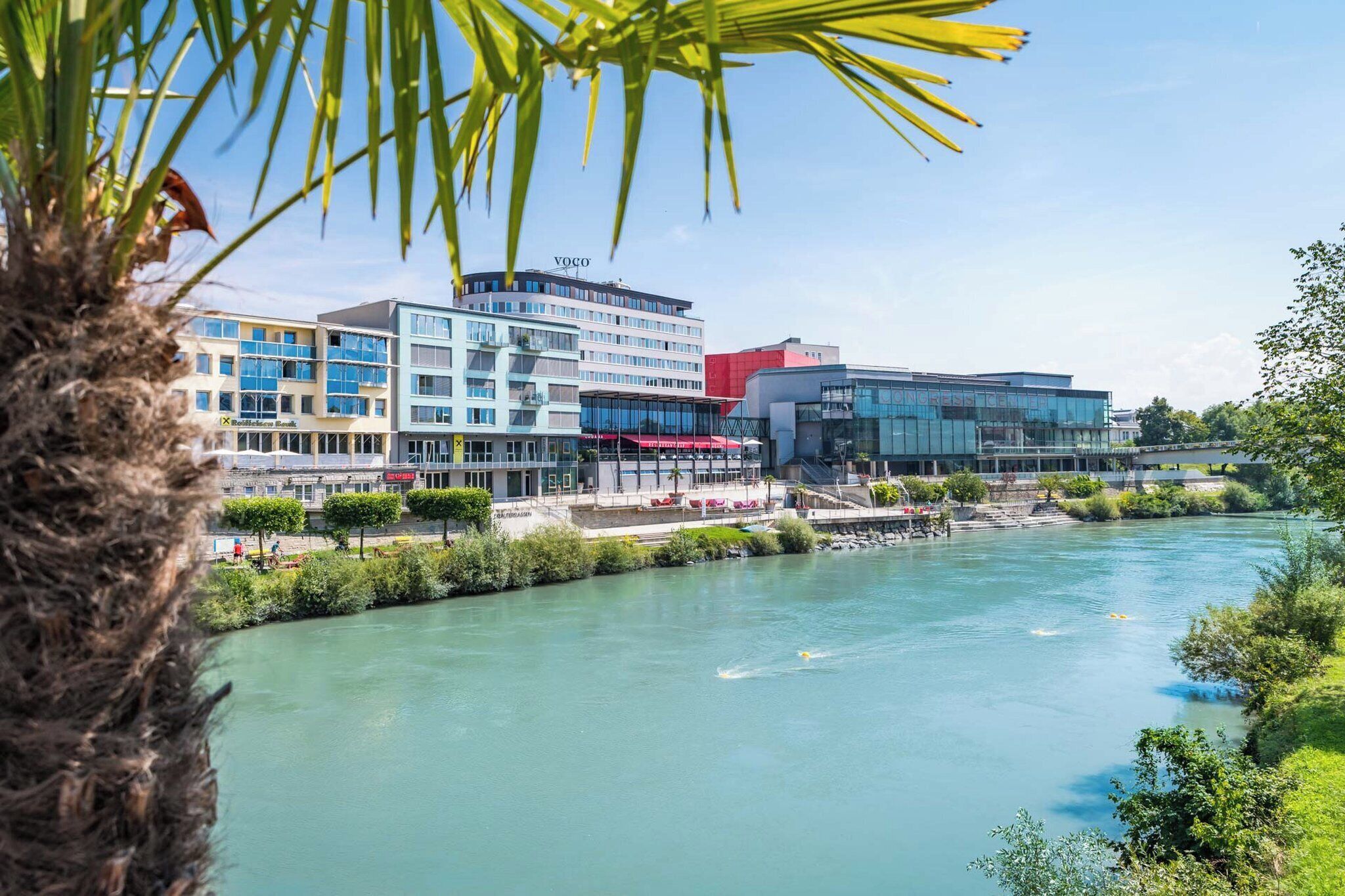 A river with buildings in the background, including a modern structure with a glass facade.
