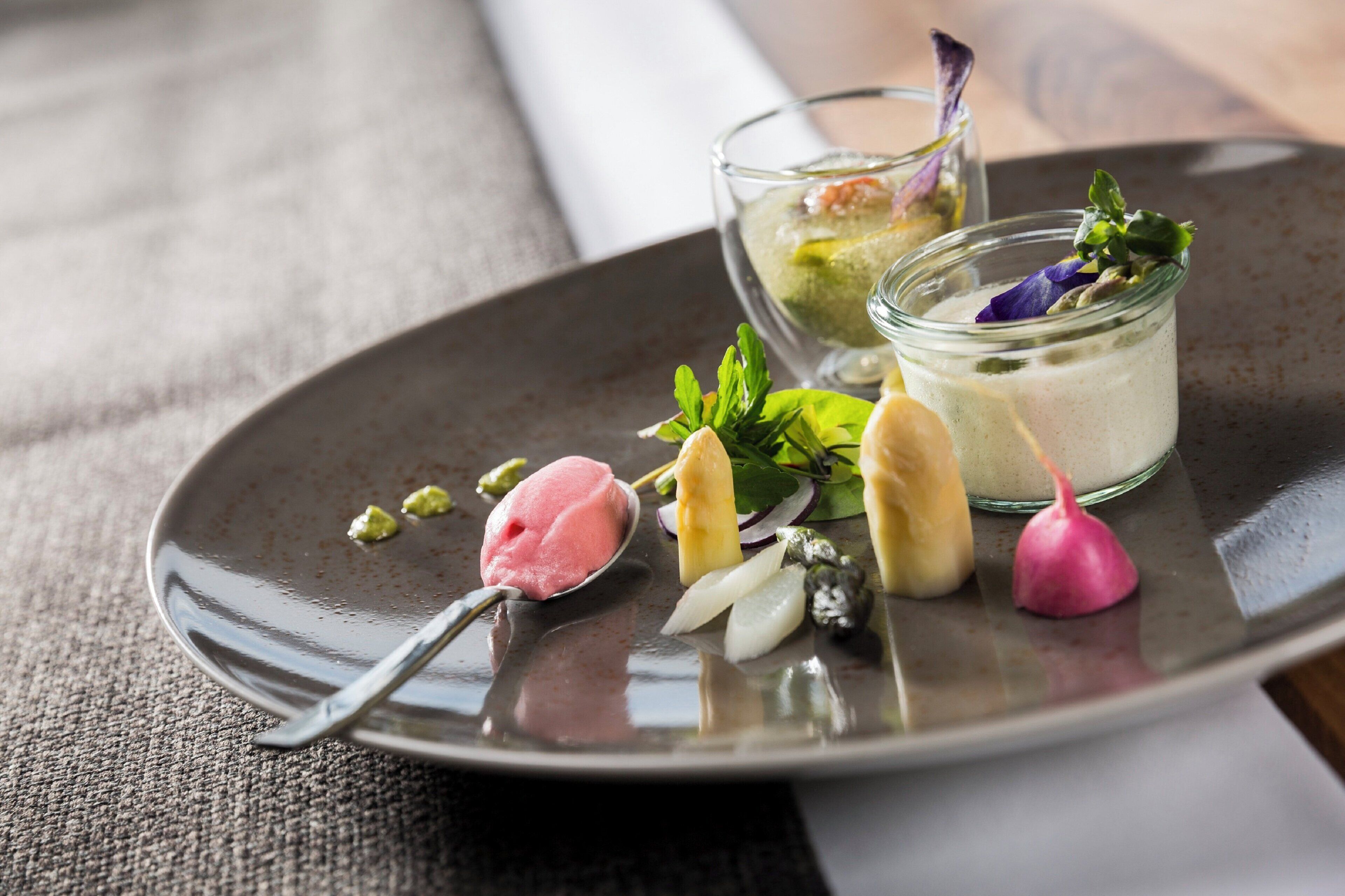 A dessert plate with various items including a scoop of ice cream, a glass of a creamy beverage, and garnishes like a radish and herbs.