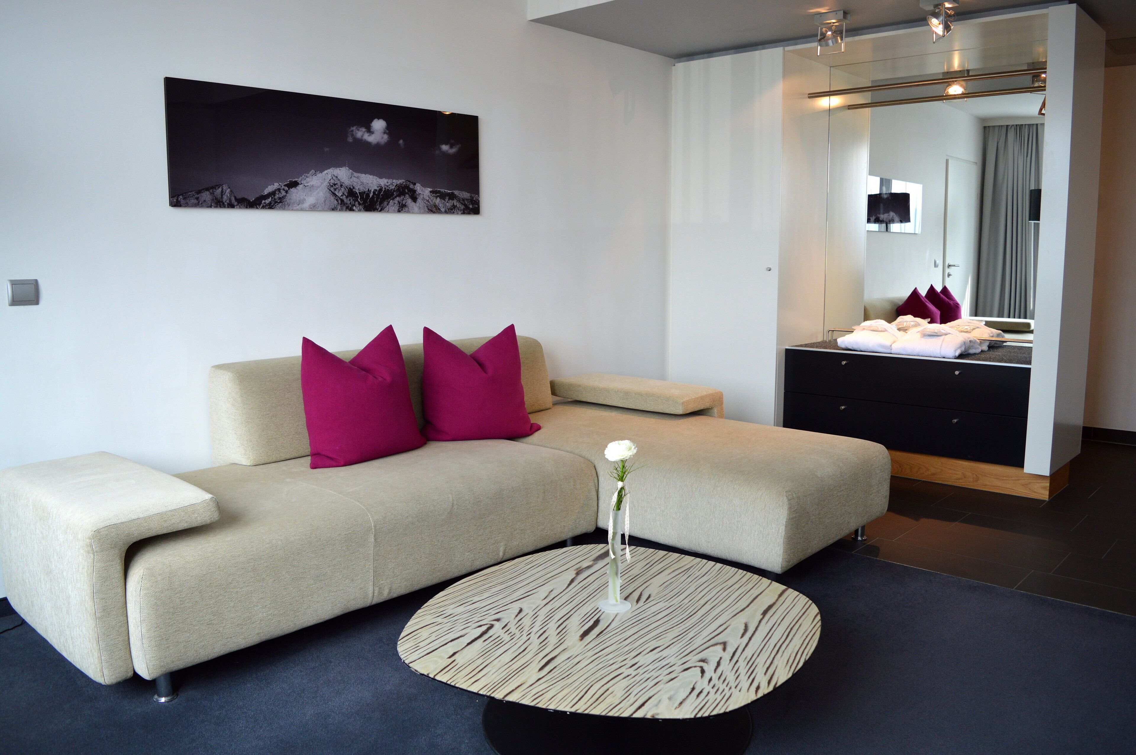 A modern hotel room with a sofa, a round coffee table, and a large mirror.
