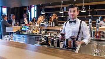 A bar area with a bartender holding a wine glass, bar equipment, and bottles.