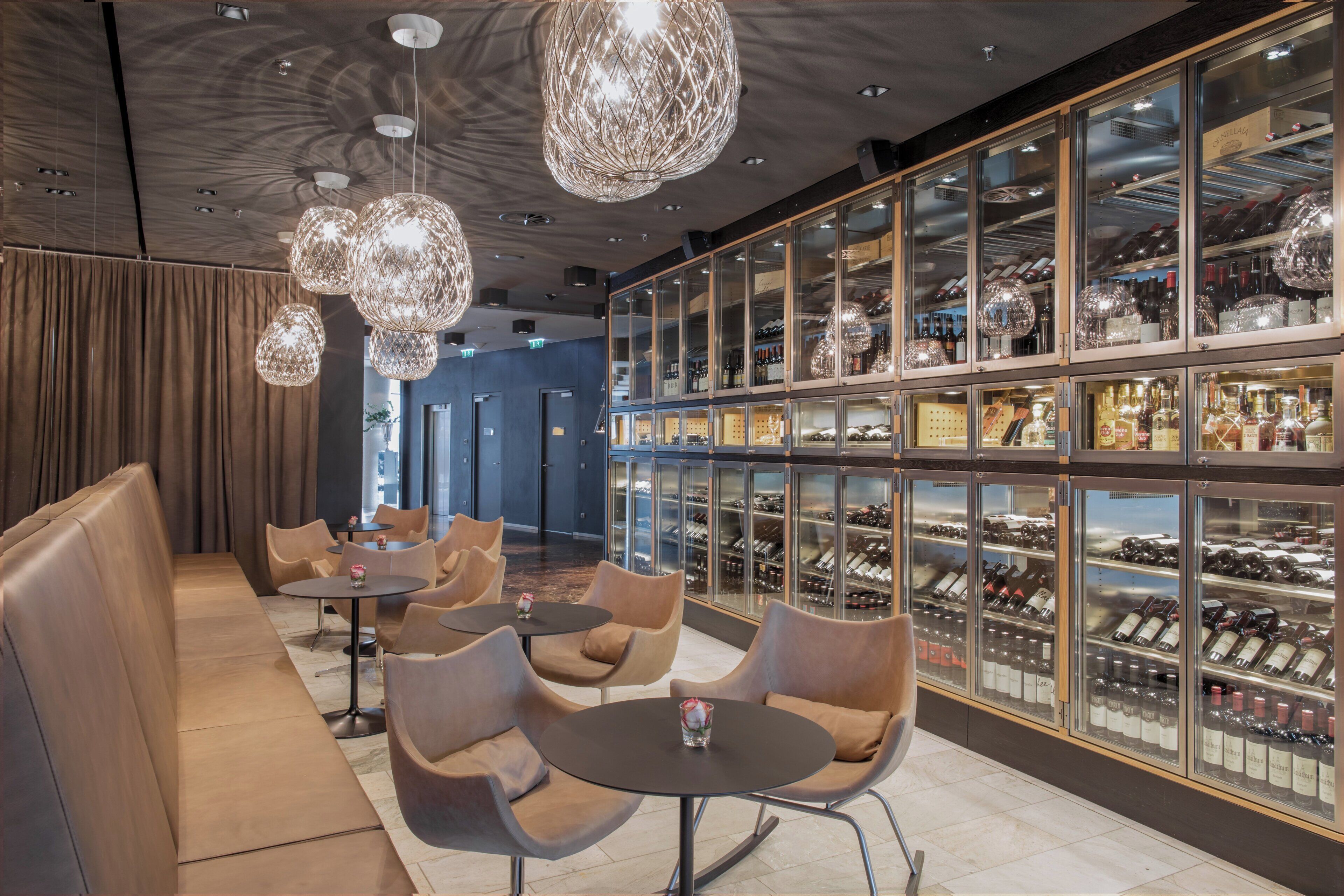 A modern bar area with leather seating, hanging crystal chandeliers, and glass-fronted wine racks.