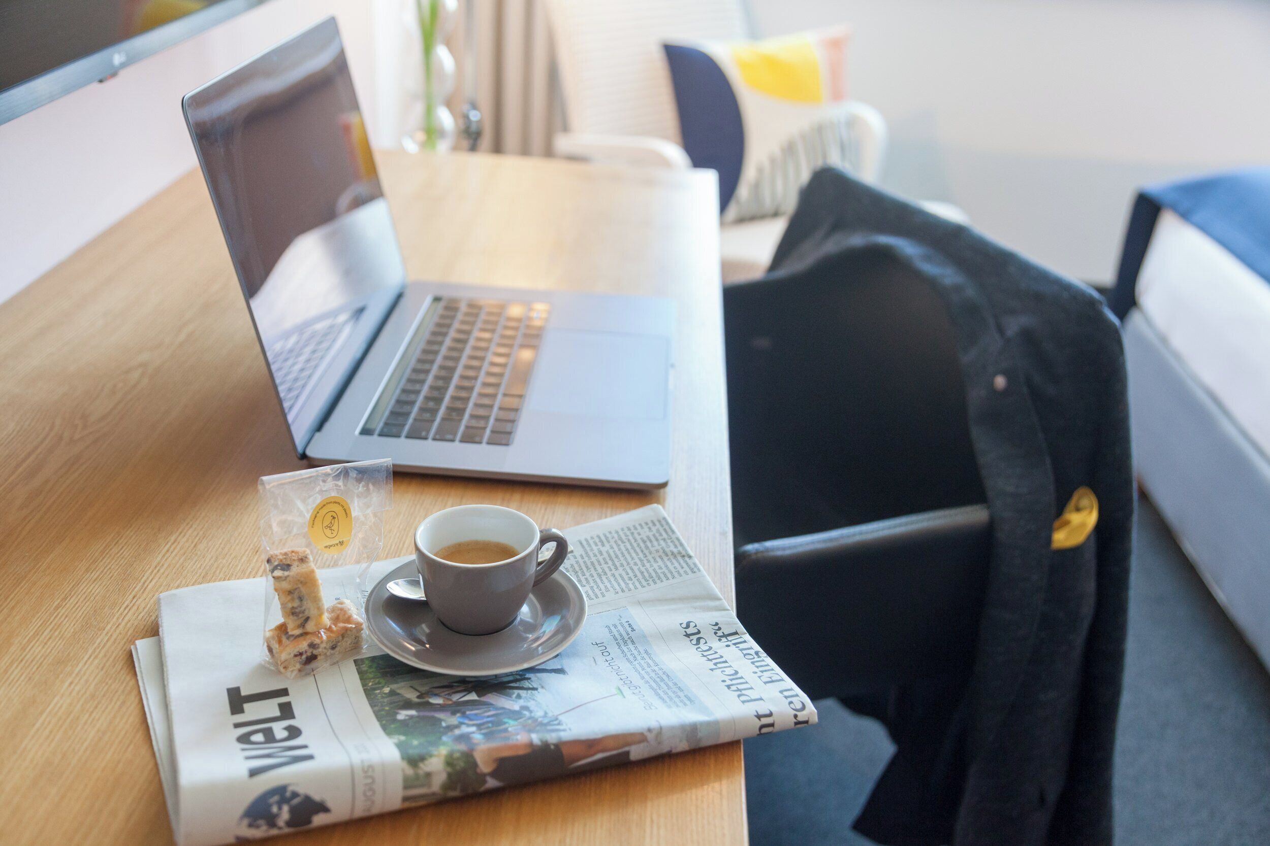 Ein Laptop auf einem Holztisch mit einer Tasse Kaffee, einem Sandwich und einer Zeitung.