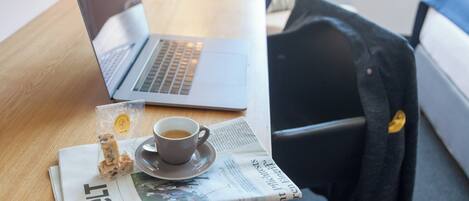 Una computadora portátil sobre una mesa de madera con una taza de café, un sándwich y un periódico.
