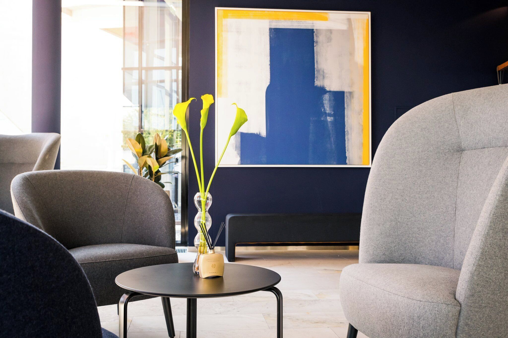 Un intérieur moderne avec une table ronde, deux fauteuils gris et un vase rempli de fleurs jaunes.