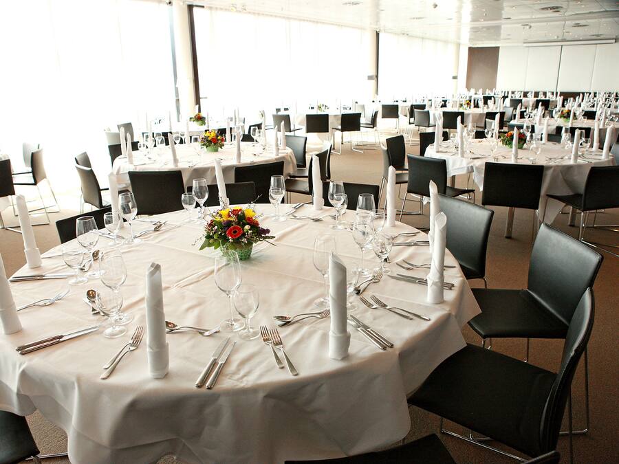A banquet hall with round tables set for a formal event, featuring white tablecloths, black chairs, and floral centerpieces.