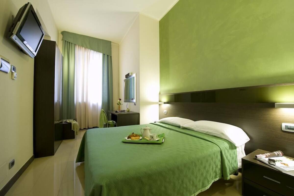A hotel room with a bed, a nightstand, a television, and a window with curtains.