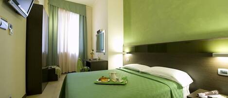 A hotel room with a bed, a nightstand, a television, and a window with curtains.