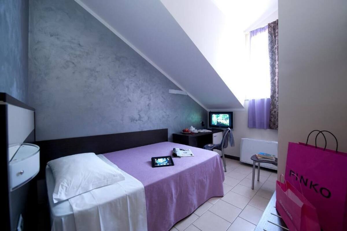 A bedroom with a bed, a desk, a television, and a window with curtains.