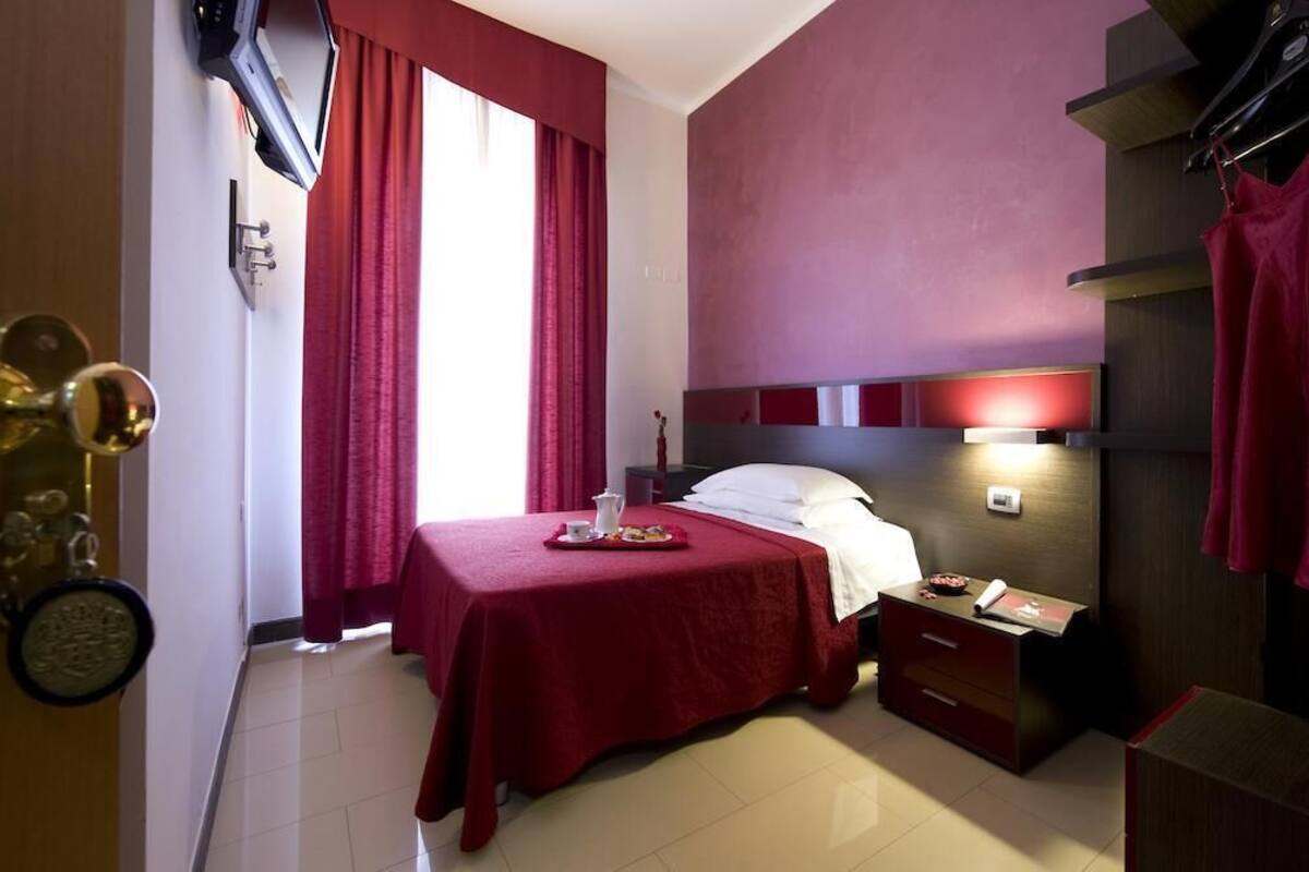 A hotel room with a bed, bedside table, and a TV mounted on the wall.