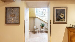 A hallway with a marble floor leading to a staircase. There are two framed artworks on the walls and a potted plant on a small table. - Boutique Hotel Dieci (Milan)