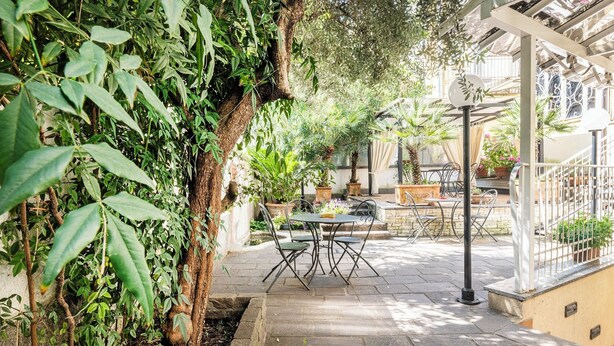 An outdoor patio area with stone flooring, metal chairs, and tables. There are potted plants and a pergola structure. - Boutique Hotel Dieci (Milan)