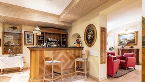 A bar area with wooden stools, a bar counter, and a dining table with chairs. There are framed pictures and a chandelier on the walls. - Boutique Hotel Dieci (Milan)