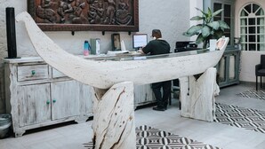 A reception desk with a large wooden carving above it, a white boat-shaped counter, and patterned floor tiles.