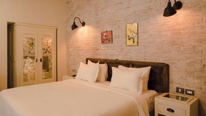 A bedroom with a brick wall, a wooden headboard, a bed with white linens, a nightstand, and two wall-mounted lamps.