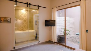 A modern bathroom with a glass-enclosed shower, a mounted TV, and a view of an outdoor seating area.