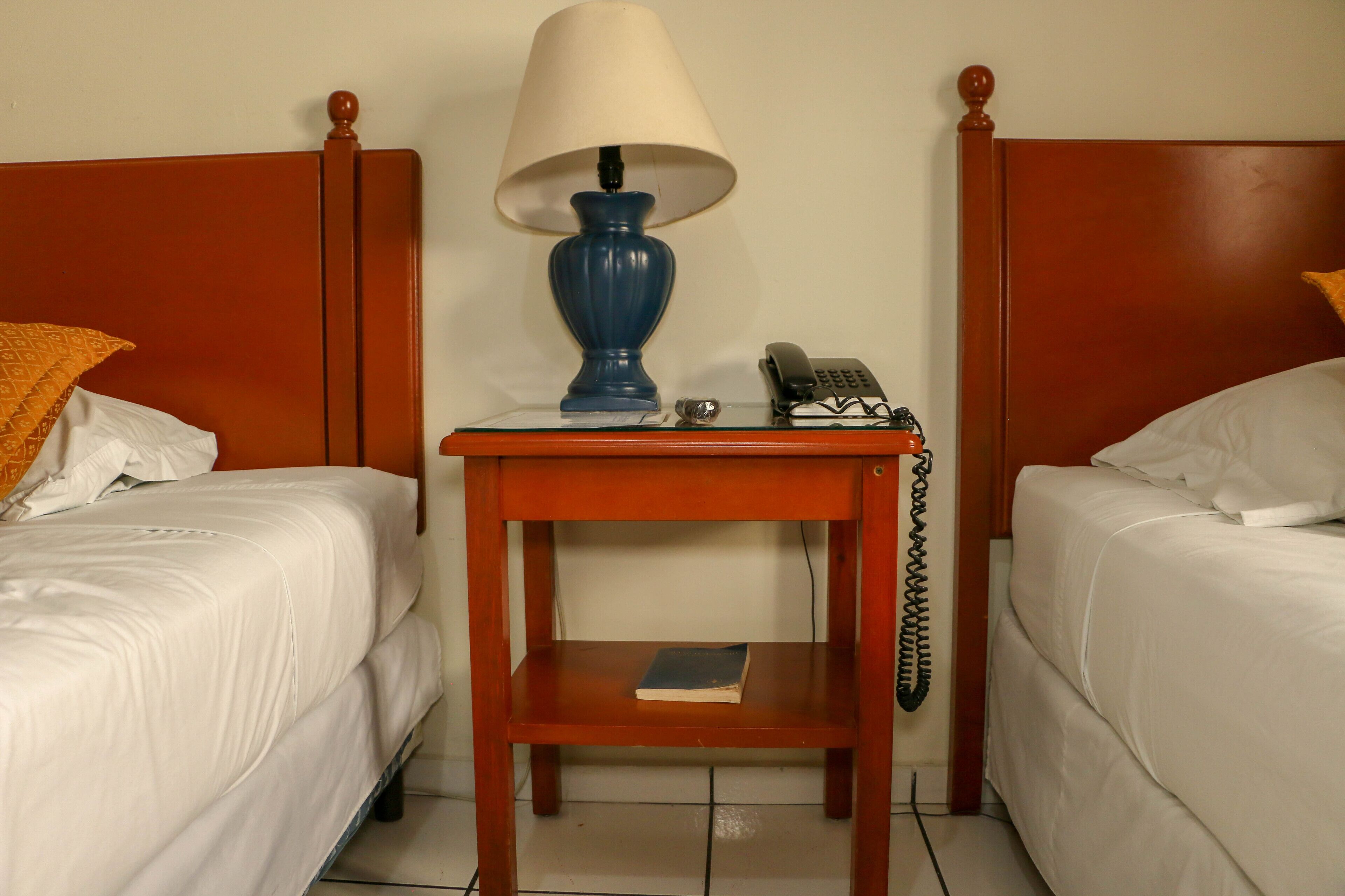 Una camera d'albergo con due letti singoli, un comodino con lampada, un telefono e un libro sul comodino.