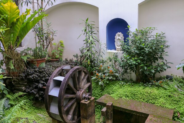 A courtyard with a water wheel, potted plants, and a statue.