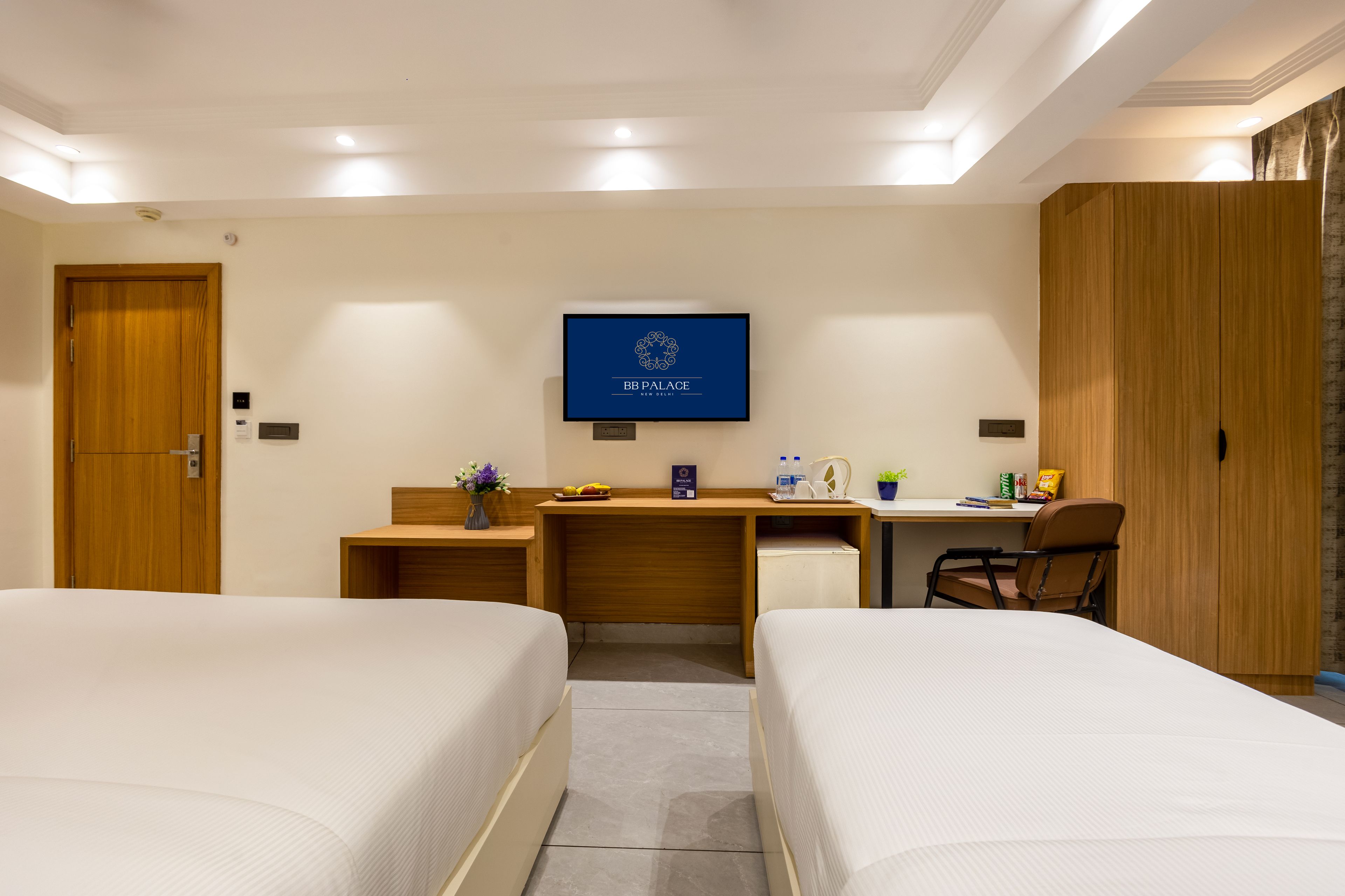 Ein Hotelzimmer mit zwei Betten, einem Schreibtisch, einem Sessel, einem Fernseher und einem Kleiderschrank.