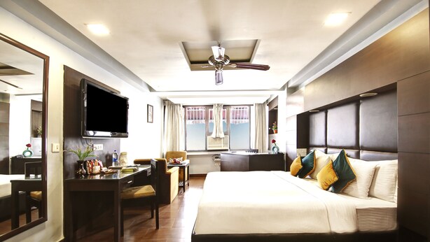 A hotel room with a bed, desk, chair, television, and a window with curtains. - Hotel BB Palace (New Delhi)