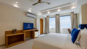 A hotel room with a bed, a desk with a TV, an air conditioner, and a window with curtains.