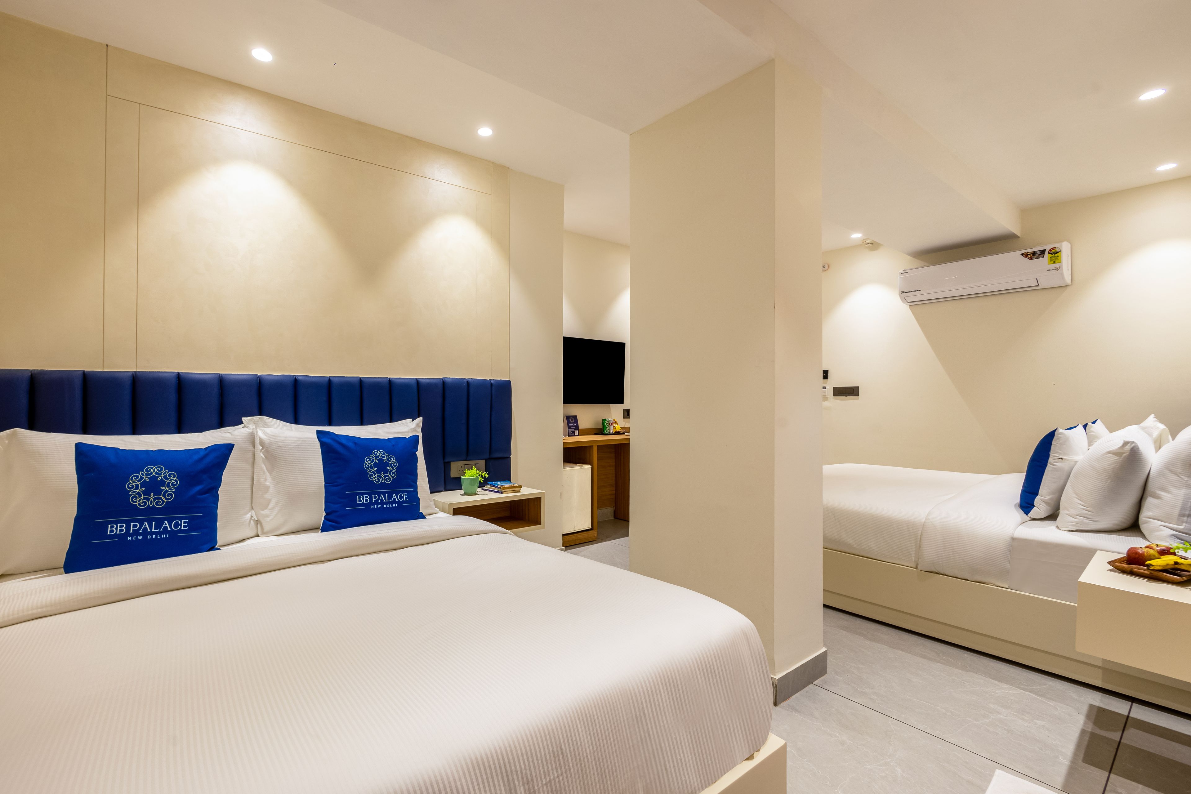 A hotel room with two beds, a bedside table, a small desk, and an air conditioning unit.
