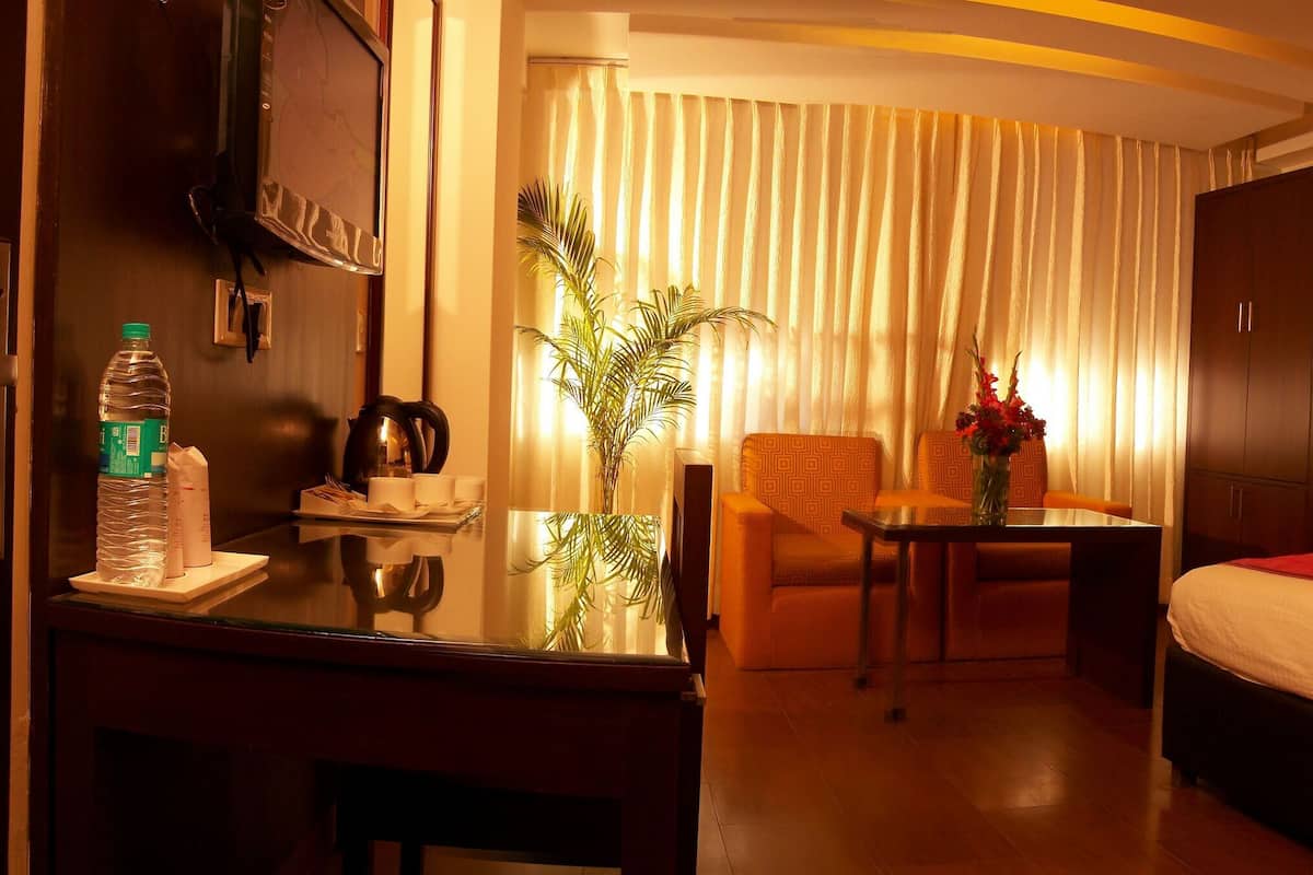 A hotel room with a bed, a desk, a chair, a table, and a potted plant.
