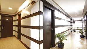 A hallway with a wooden floor, a dark door, and potted plants. - Hotel BB Palace (New Delhi)