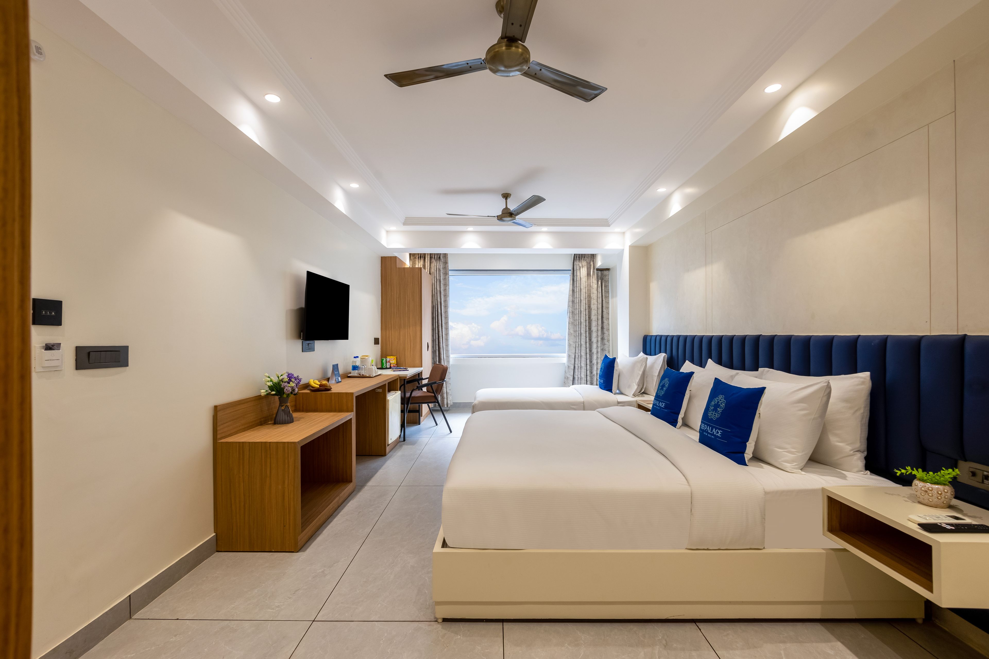 A modern hotel room with a large bed, a desk, a flat-screen TV, and a ceiling fan.