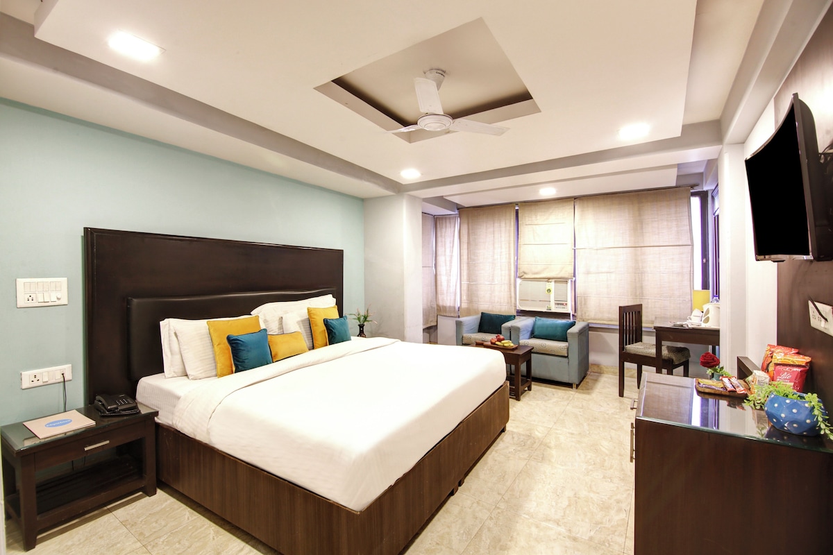 A hotel room with a large bed, bedside tables, a desk, a chair, and a television.