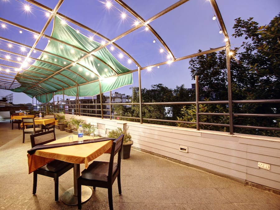 Um pátio externo com mesas e cadeiras, coberto por um toldo verde e luzes de Natal.