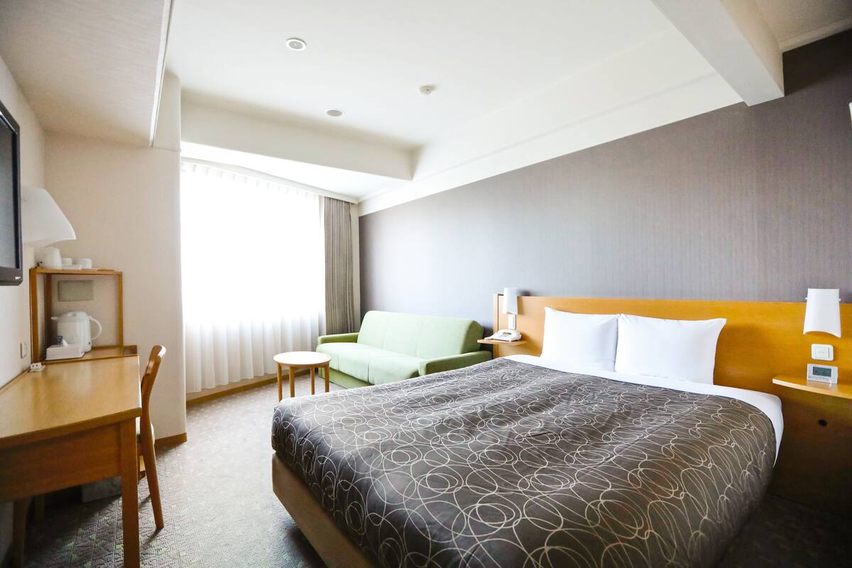 A hotel room with a bed, a desk, a chair, a sofa, and a window with curtains.
