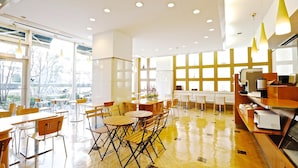 A modern dining area with wooden tables and chairs, large windows, and a kitchen area with appliances. - Tokyo Green Hotel Korakuen (Tokyo)