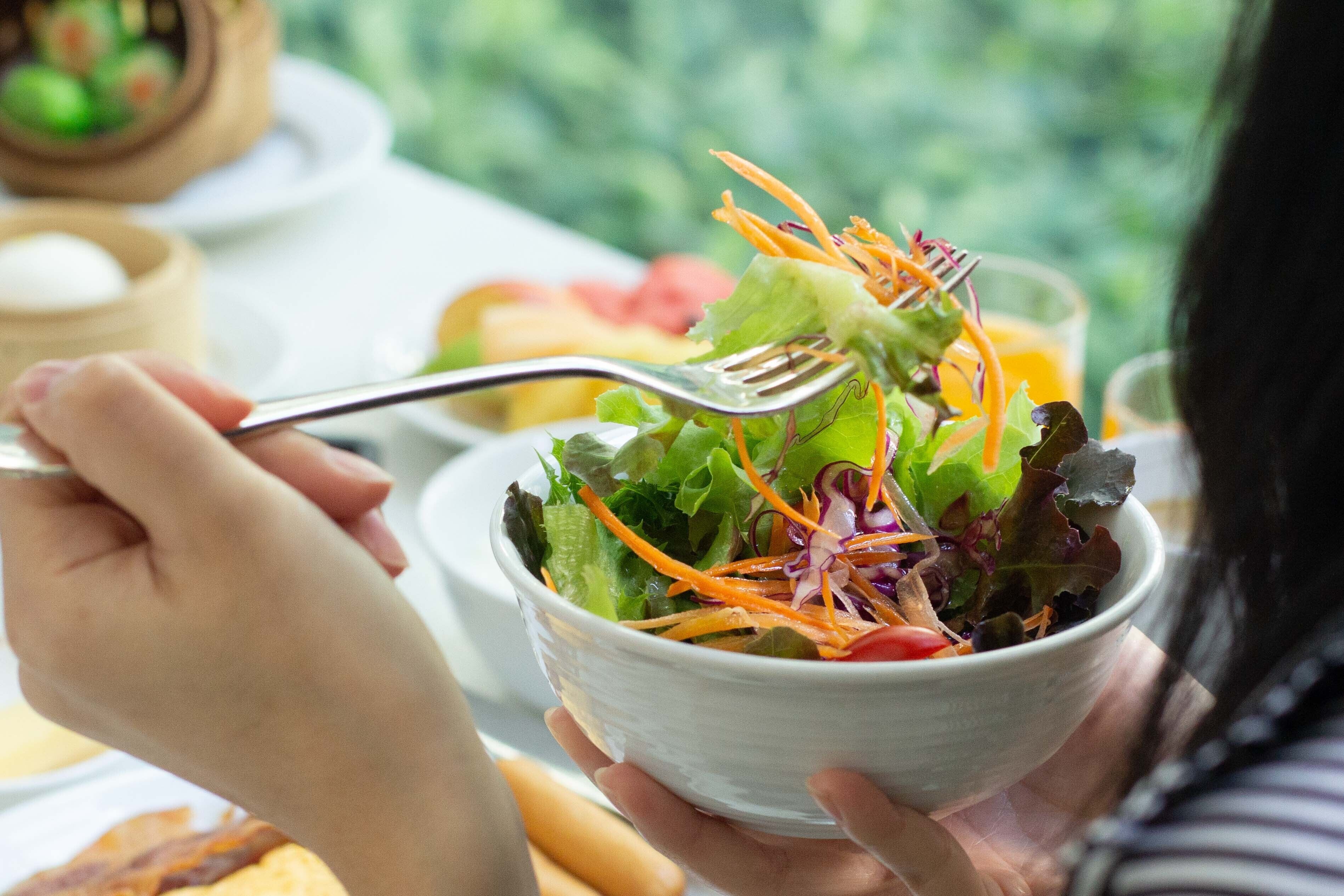 A person holding a bowl of salad with a fork.
