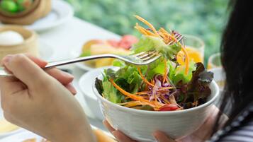 A person holding a bowl of salad with a fork.