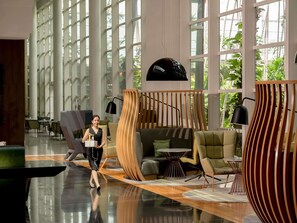 A spacious lobby with large windows, a modern sofa, a round table, and a unique wooden structure. - Pullman Bangkok King Power (Bangkok)