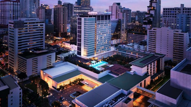 Um hotel moderno e alto com um grande letreiro 'Pullman', cercado por outros edifícios altos.