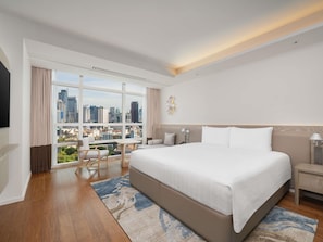 Une chambre d’hôtel moderne, dotée d’un grand lit, d’un bureau et offrant une vue sur le paysage urbain.