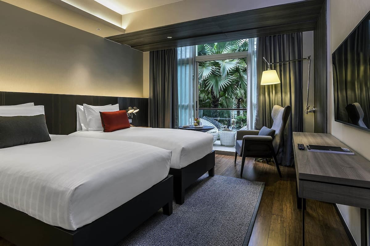Una habitación de hotel moderna con una cama grande, un escritorio y un balcón con vistas a palmeras.