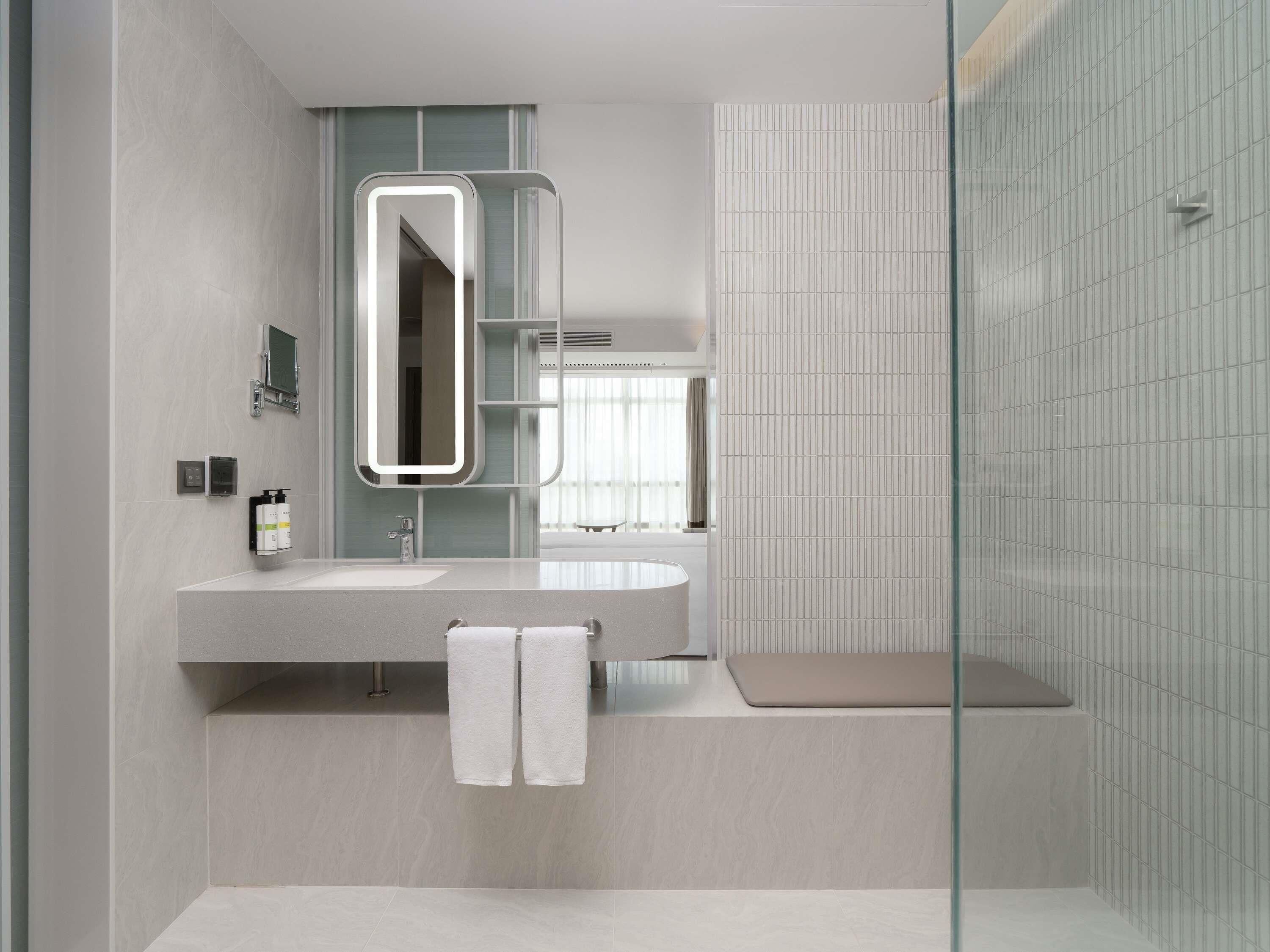 A modern bathroom with a large mirror, a sink, and a shower area.