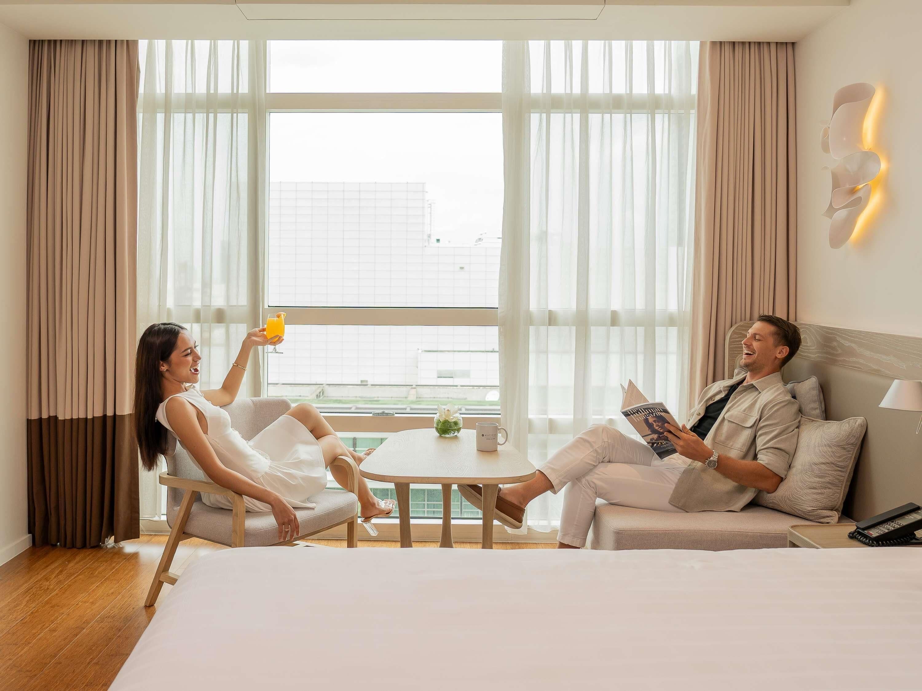 A hotel room with a bed, two sofas, a small table, and a window with curtains.