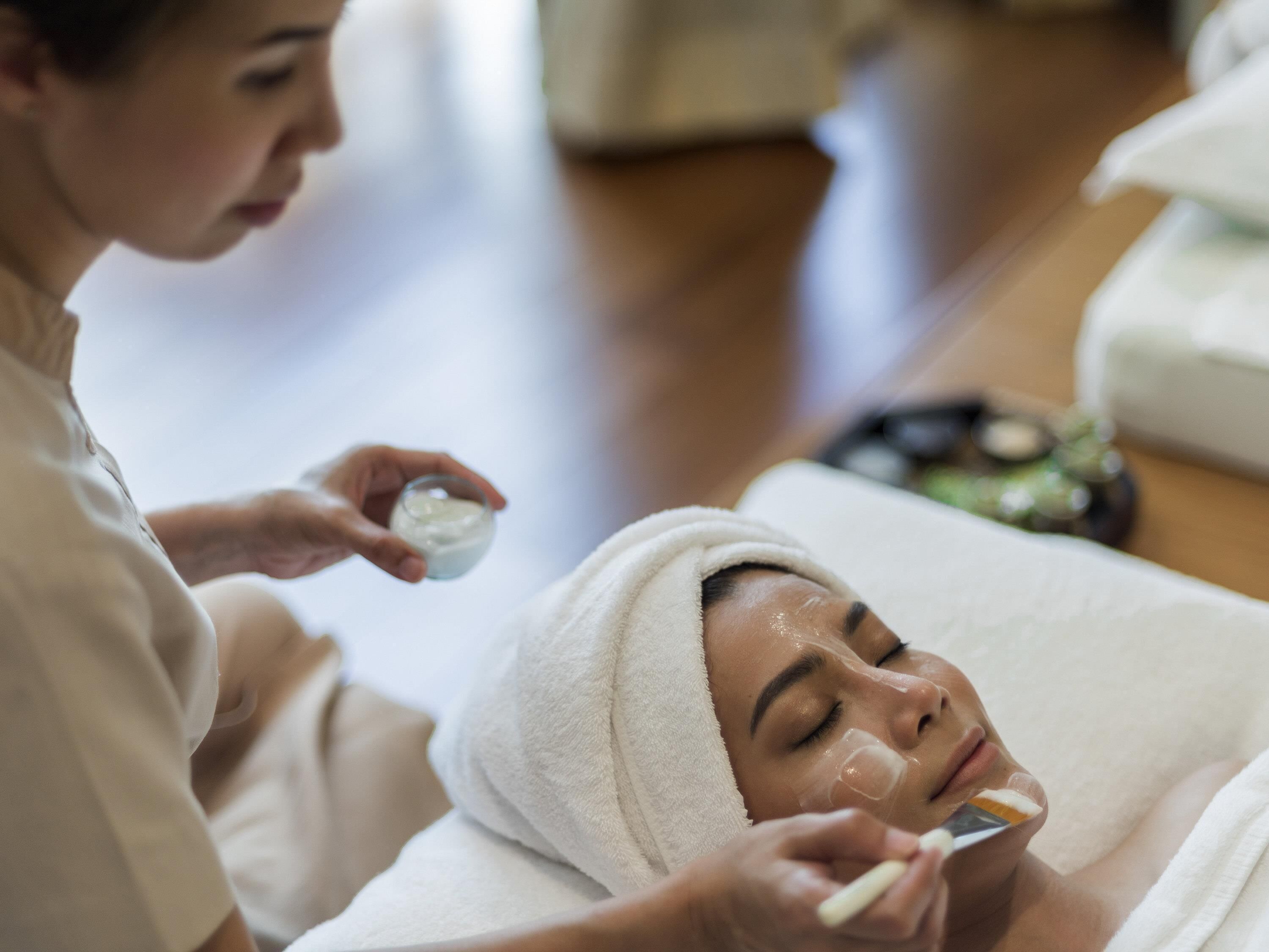 A person receiving a facial treatment in a room with a wooden floor and a white towel.