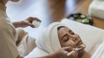 A person receiving a facial treatment in a room with a wooden floor and a white towel.