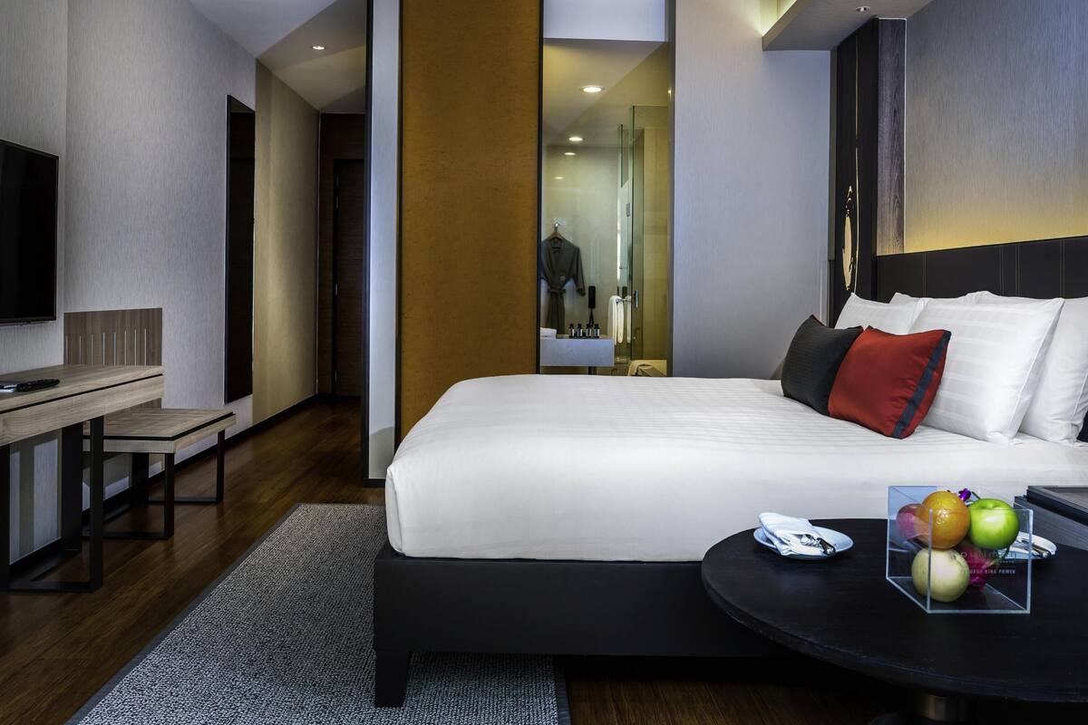 Una habitación de hotel moderna con una cama, un escritorio, un televisor y una pequeña mesa con fruta.